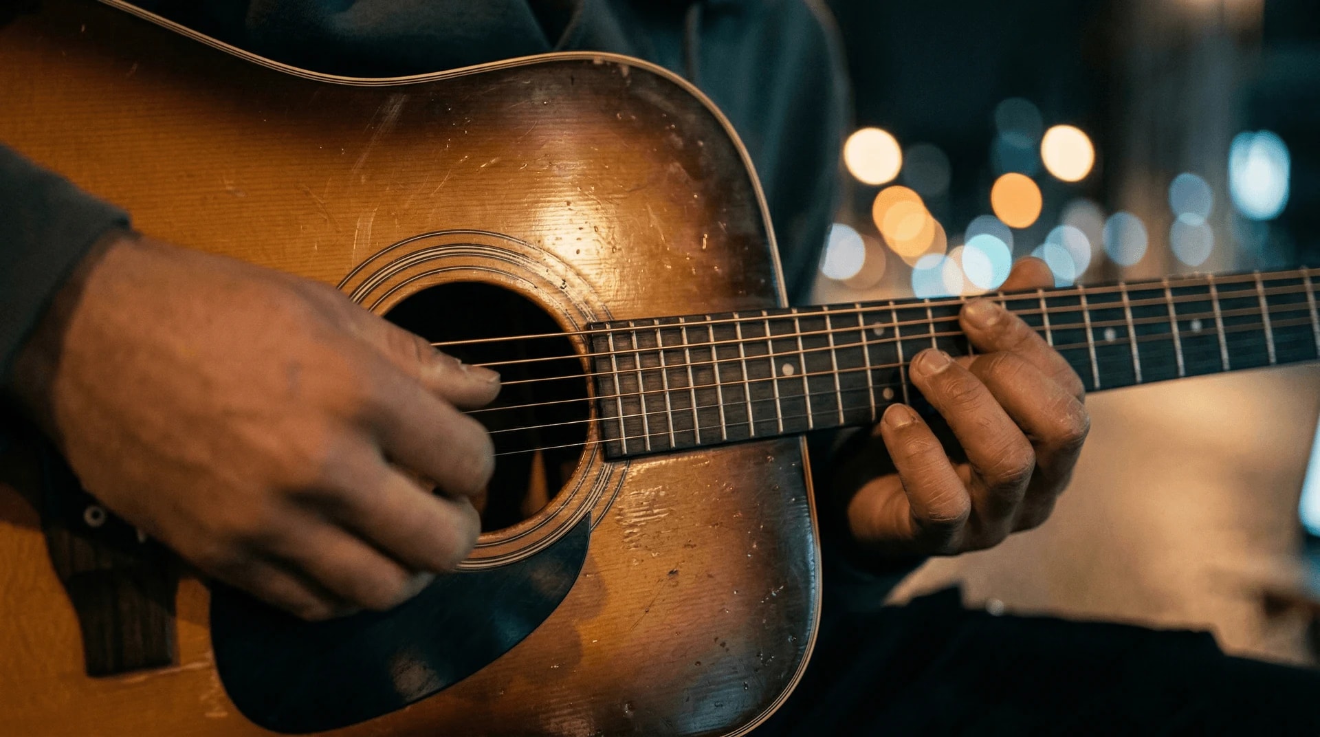 Still from the film: close on hands playing an acoustic guitar, stage lights behind.